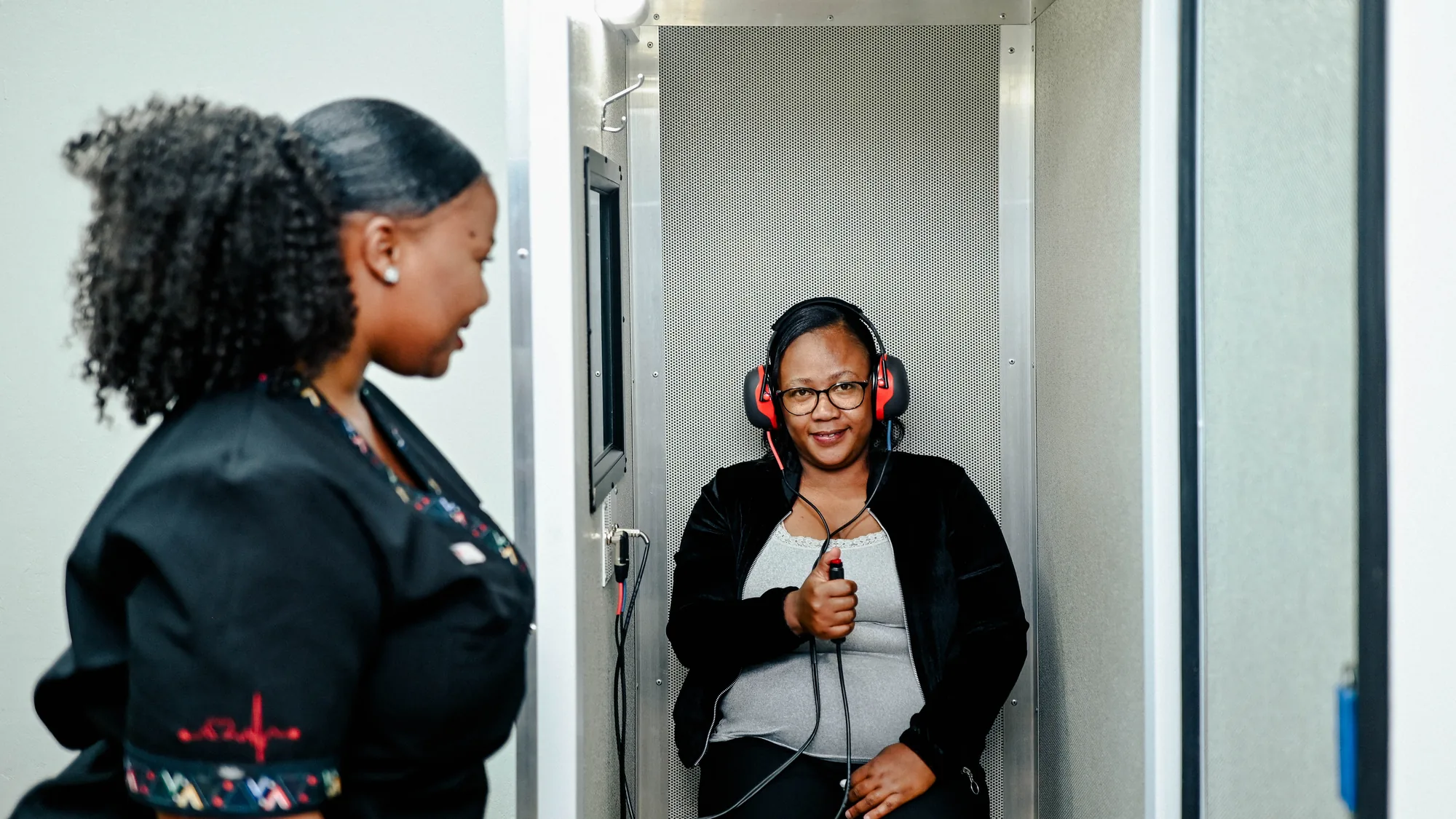 A Care Net nurse observing while a worker responds during a hearing test in the audiometry booth.